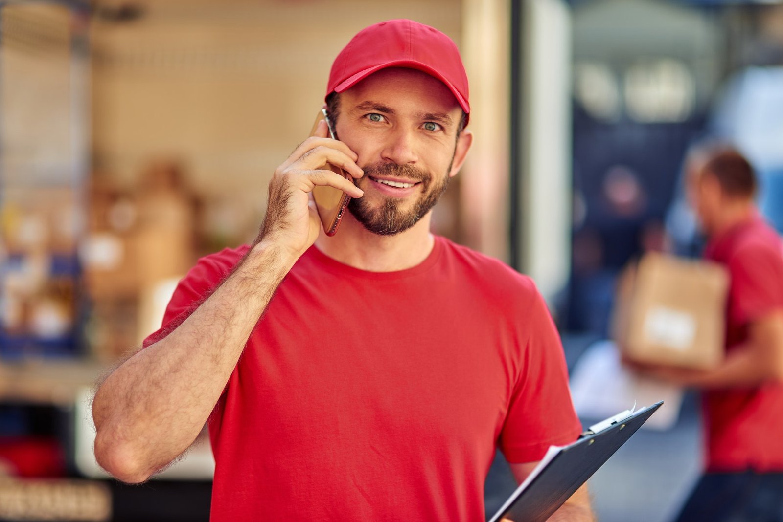 young cheerful caucasian male courier in red uniform talking on phone.jpg