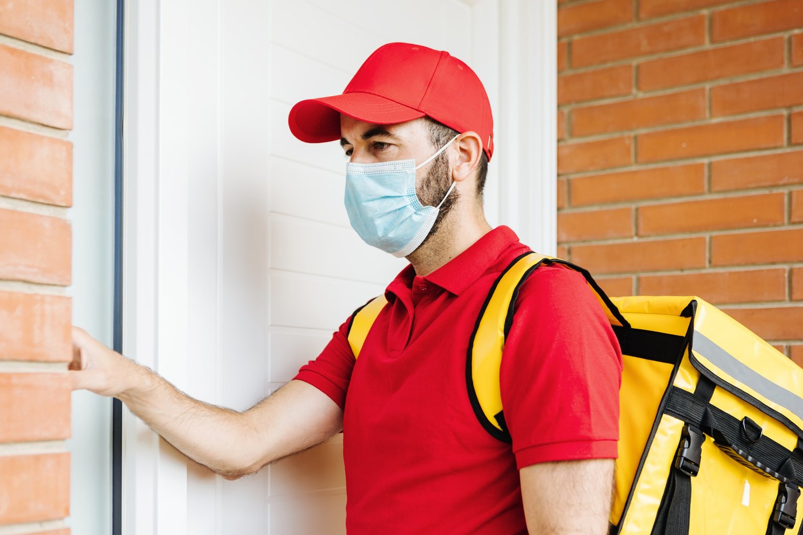 young hispanic delivery food man in face mask ringing the doorbell food delivery concept.jpg